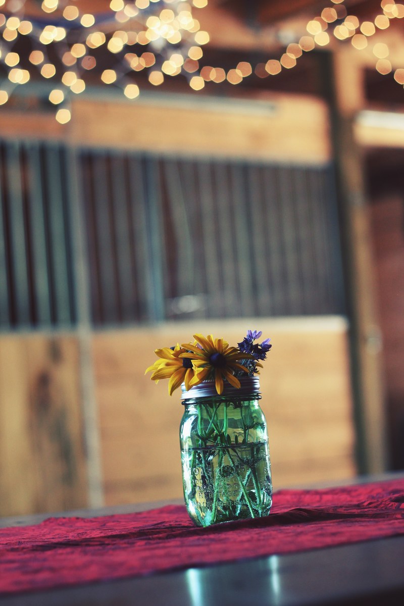 a glass jar with yellow and violet flowers on a wooden surface, modest flower jar 4k