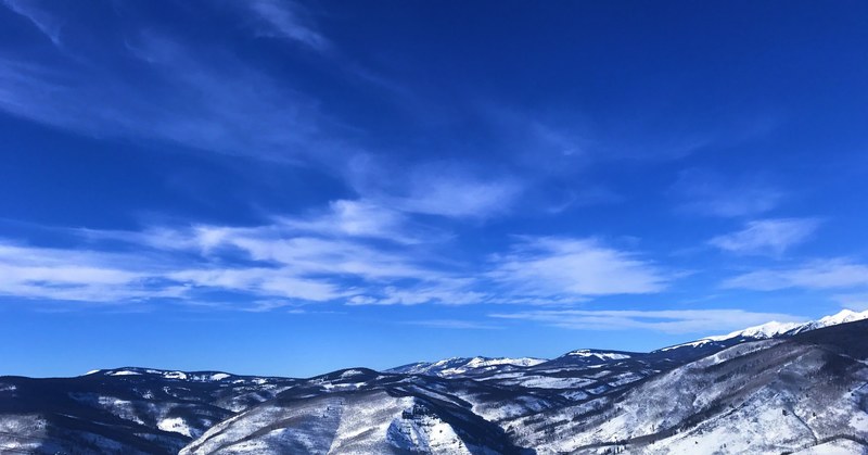 a low snow capped mountain range under a blue sky, blue skies and patchy clouds 4k