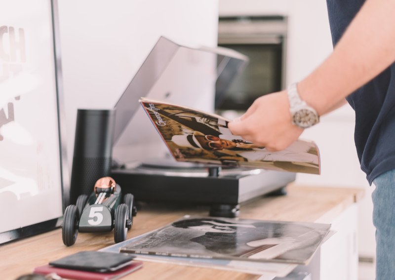 man reading vinyl sleeve over a table with a record player and toy car on it, man reading vinyl record 4k