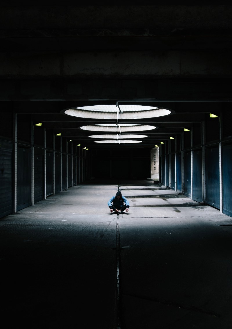 a man in a hoodie sits on the floor of a deserted parking lot in london, _man parking lot london 4k