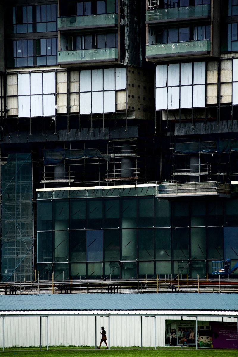a woman is walking through a covered walkway below a tall building under construction in singapore, _constructive 4k