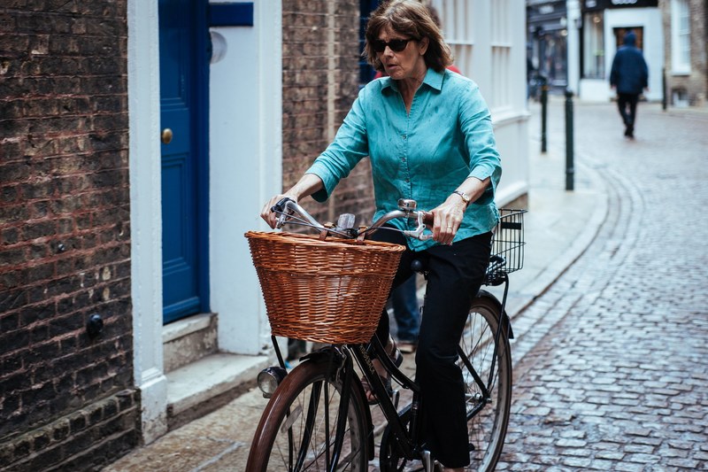a middle aged woman in a blue shirt riding a bicycle on a cobbled street, lady on a bike 4k