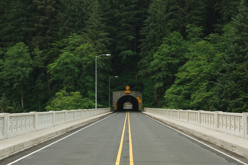 empty bridge road leads to a tunnel through the forest, oregon coast tunnel 4k