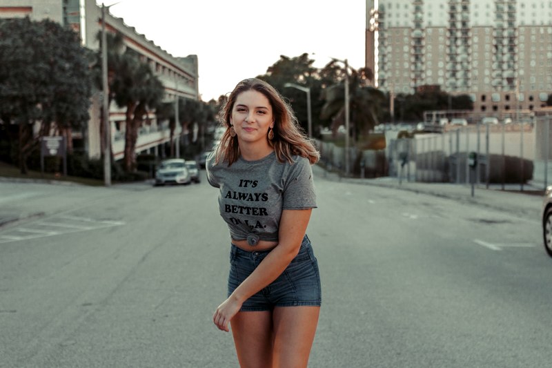 a woman stands in the street wearing a shirt reading quotits always better in laquot, its always better in la_ 4k