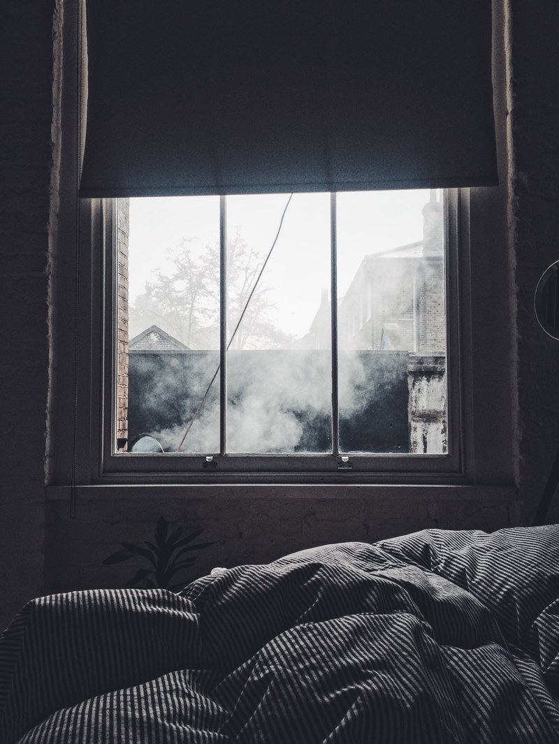 interior of a bedroom with a blanket and a window showing smoke and other houses outside, bedroom window 4k