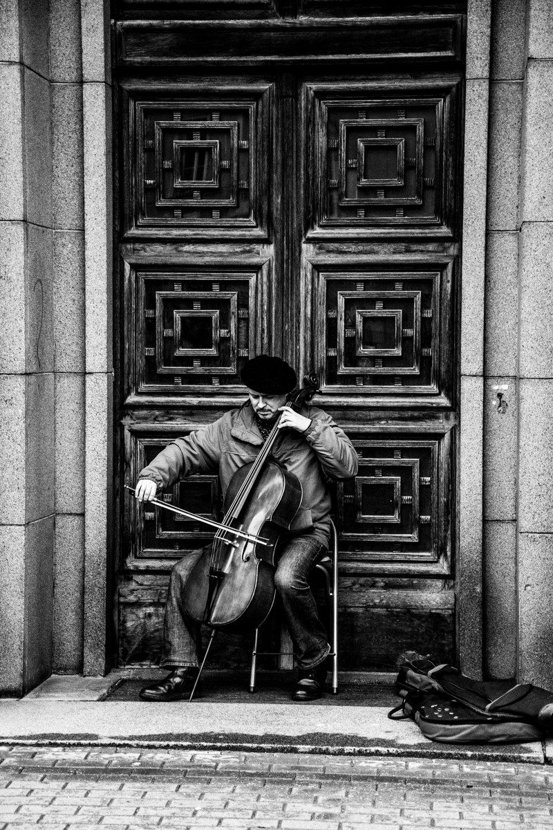 black and white shot of street musician performing with cello in doorway in riga, music on the streets of riga 4k