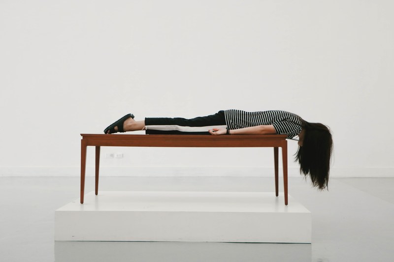 lady at the bangkok art and culture centre lays on stomach on a wood table, a woman lies face down on a table 4k