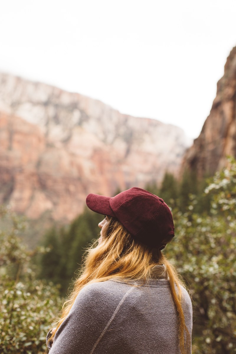 woman in a red baseball cap looking out at scenic mountains, mountain hike alone 4k
