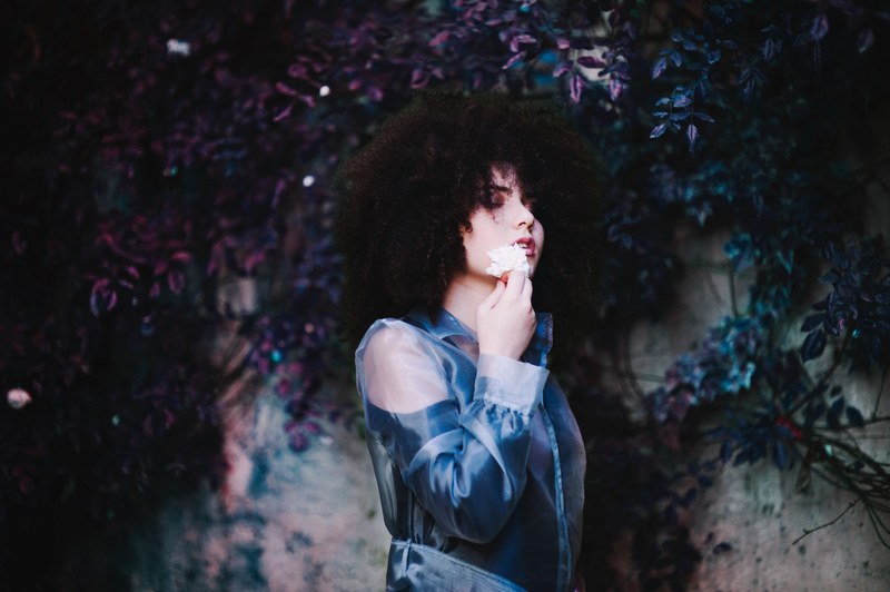 serene woman brushes flower against her cheek with eyes closed, violet dream 4k