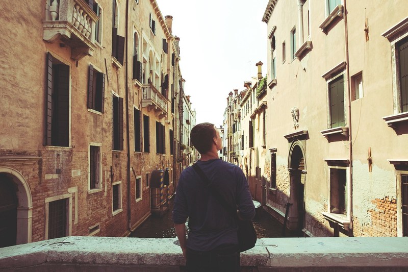 a man admiring old buildings over a canal in venice, male tourist enjoying the view in venice 4k