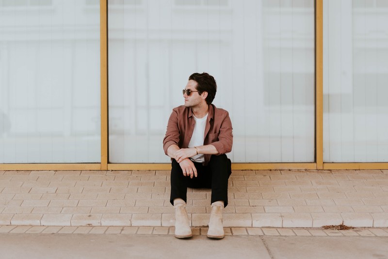 a man in boots sits on a ledge in front of plate glass windows, man sitting on window ledge 4k