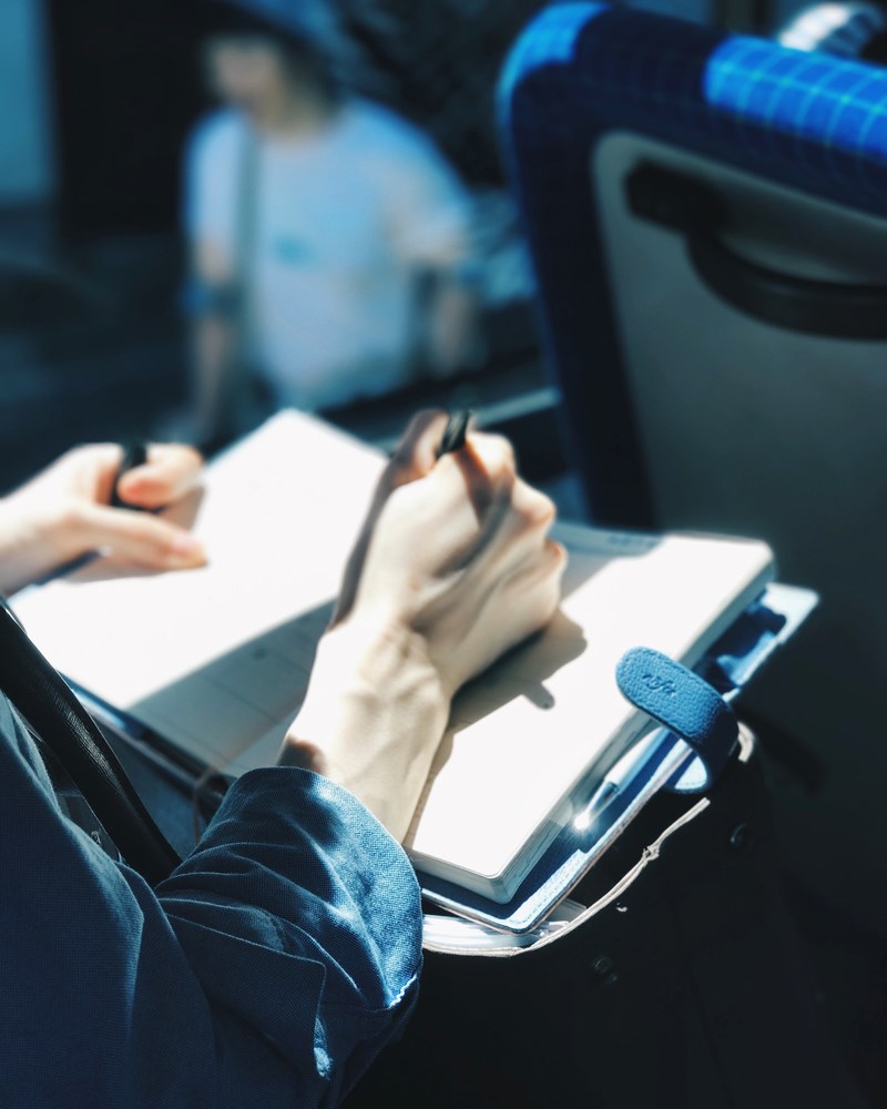a person writing in a notebook while on public transport, journaling on a bus 4k