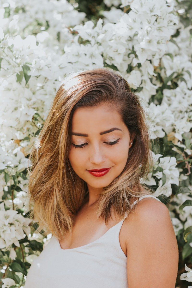 woman wearing subtle makeup smiling and looking down near white flowers alone, flowers_ 4k