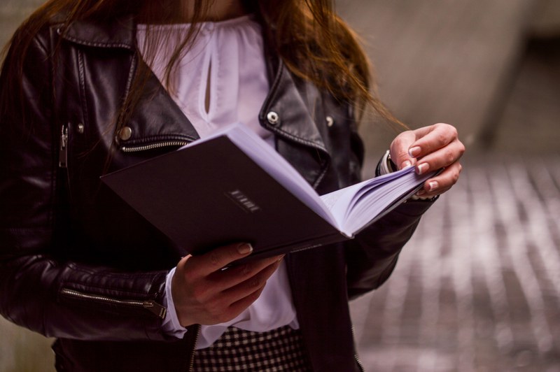 a woman in a leather jacket and white blouse holds an open book reading, woman reading a book 4k