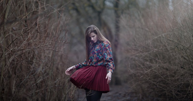 a woman looks down at her billowing skirt on a path among dead trees in vilnius, wind 4k