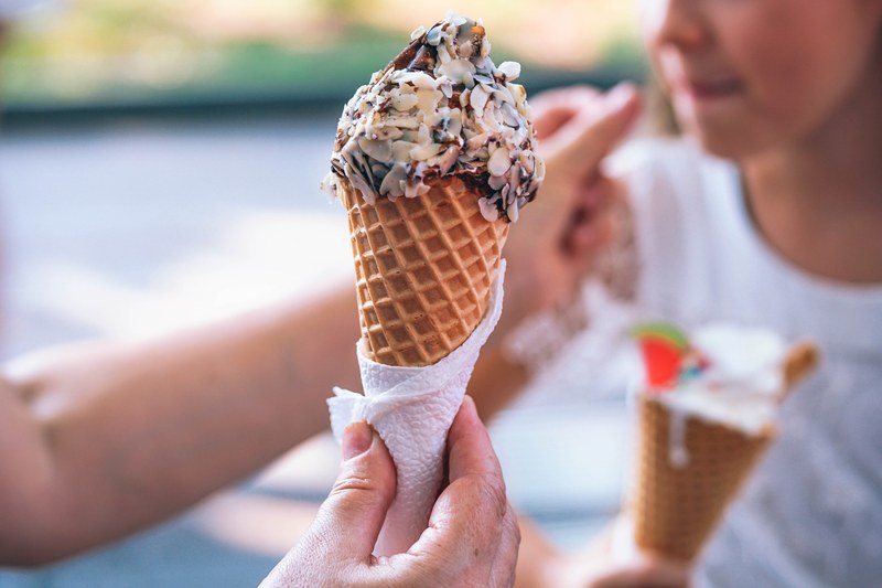 a person holding an ice cream covered in chocolate syrup and almond slivers in a waffle cone in yalta, ice cream cone 4k