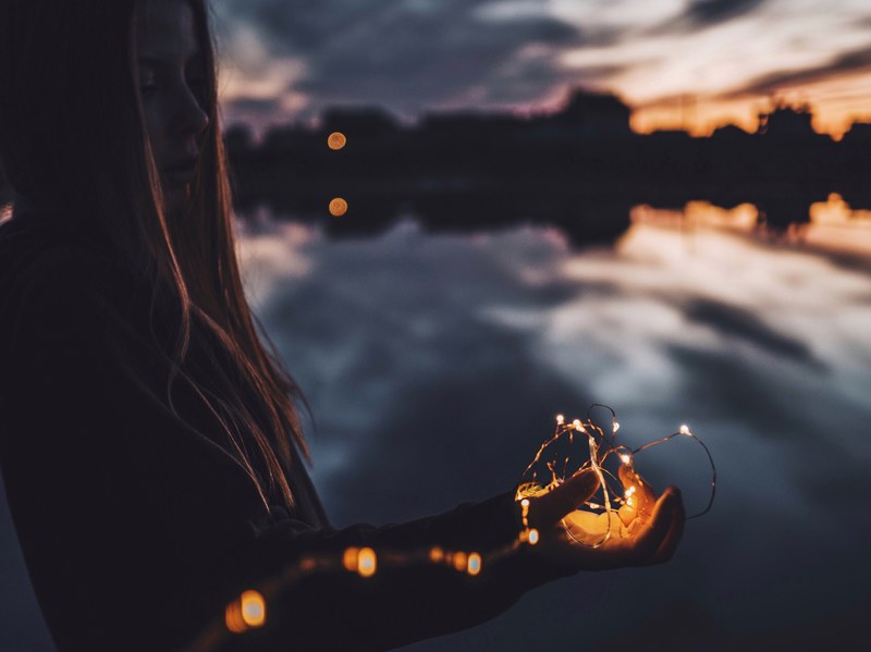 a girl holding fairy lights in her hand by a lake on an evening, lights 4k