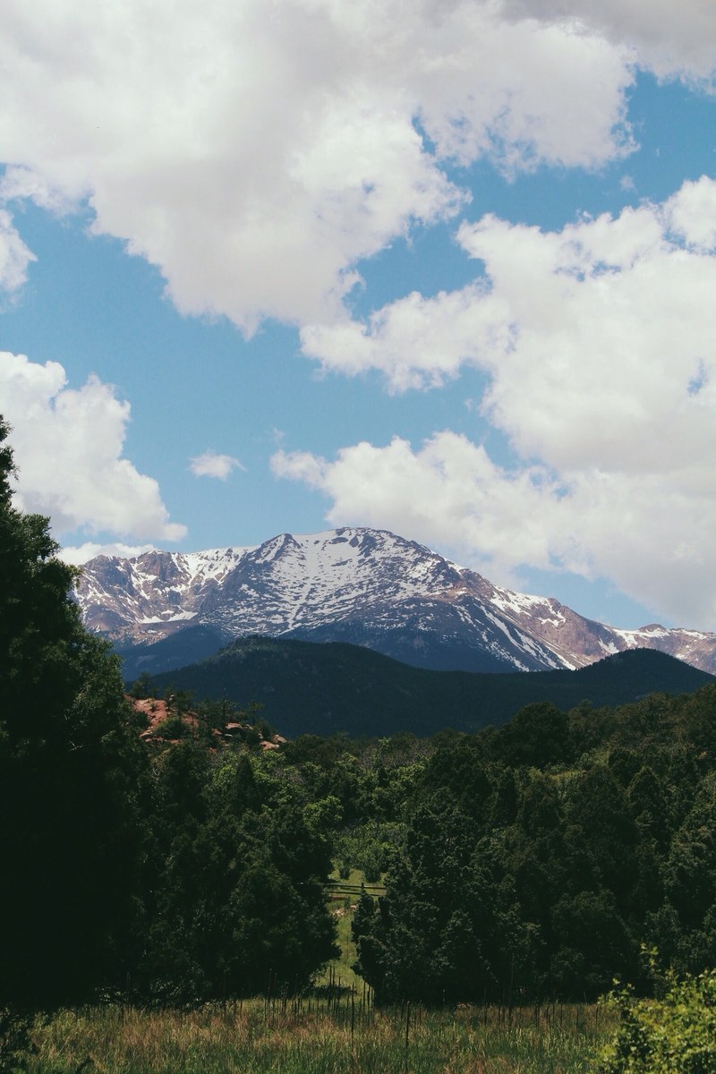 a tall snowy mountain towering over green countryside, mountain under fluffy clouds 4k