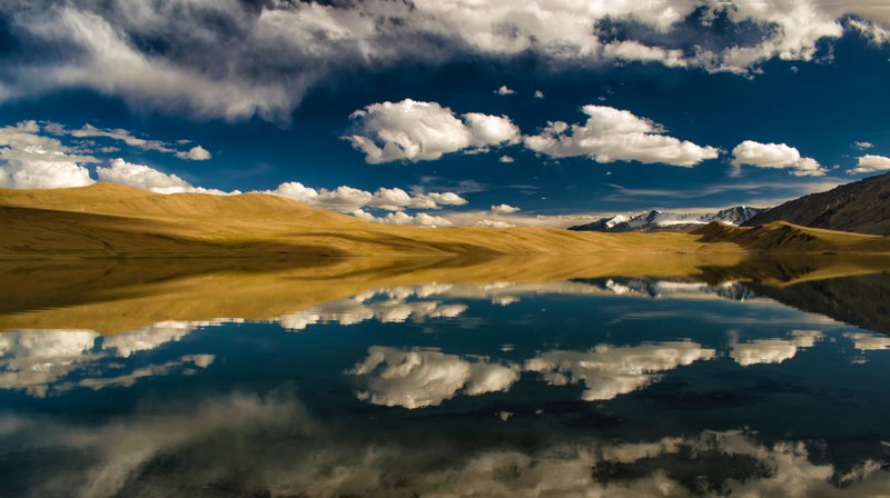 the still surface of a mountain lake reflects fluffy clouds in the sky above, perfect reflectio on tso kiagar lake 4k