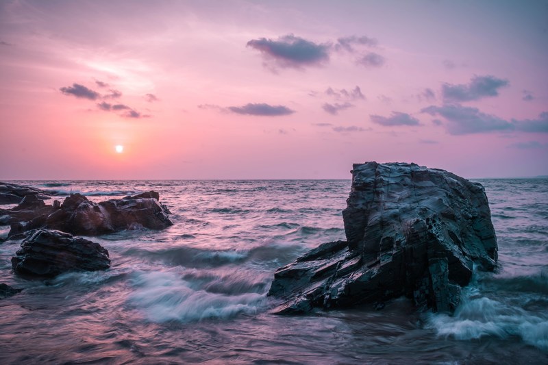 the sky is pink as the waves break on rocks at sunrise or sunset in goa, vitamin sea 4k