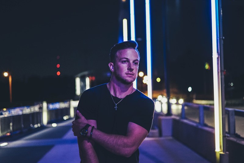 a man in a black shirt wearing a cross pendant walks down the street at night, _all of the lights 4k