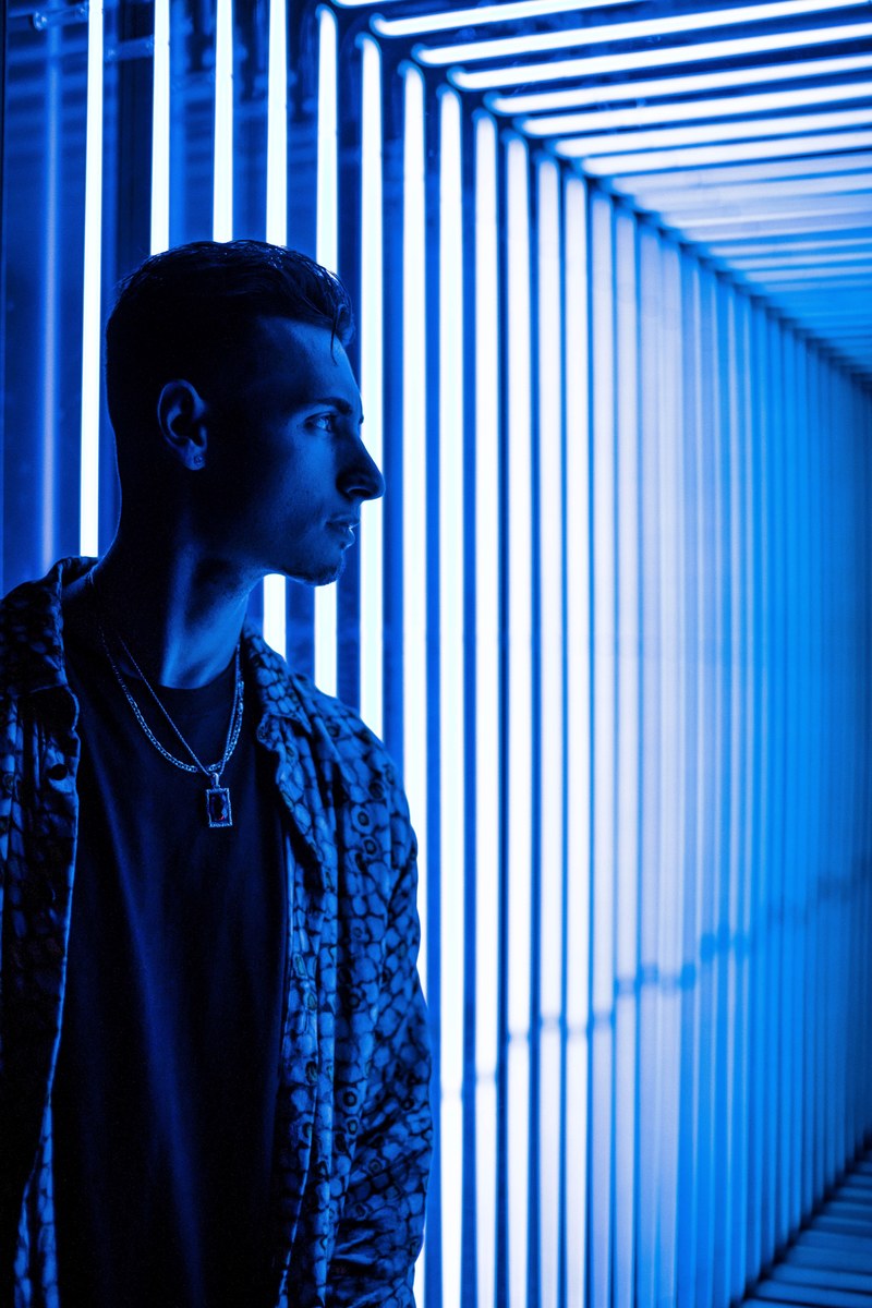 a man standing against a blue neon lighted wall in a club in new york, josh_sobel dizzy_d718 4k