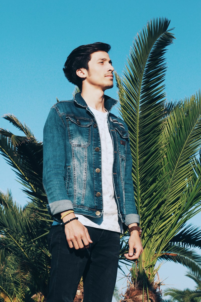 a smiling man in a jean jacket in front of a palm tree and blue sky, man with palm tree 4k