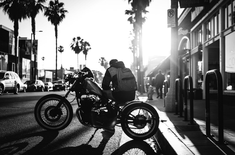 black and white shot of man with backpack sitting on motorbike with palm trees venice, abbot kinney 730 pm 4k