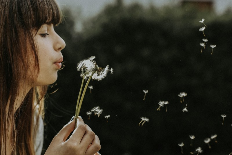 a woman with bangs blows on a dandelion scattering its seeds, whisper 4k