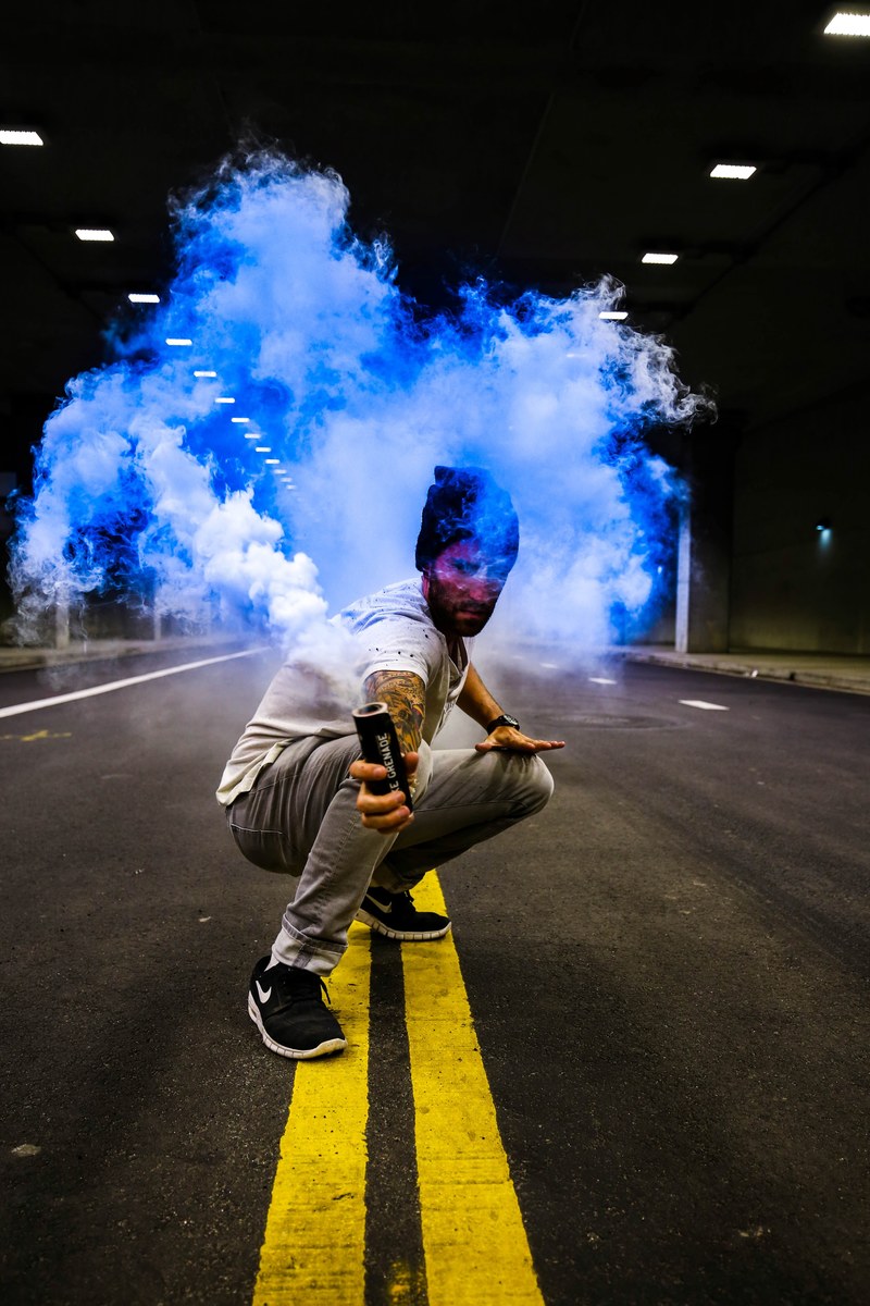 person crouching in the street holding a blue smoke grenade, let the colors out 4k