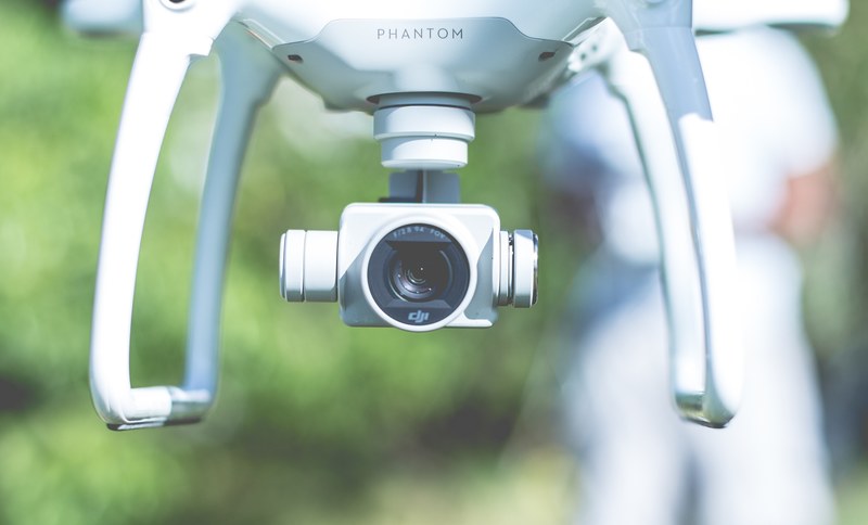 macro of a white phantom dji drone hovering in front of a green background with a man in white standing by, camera white drone 4k
