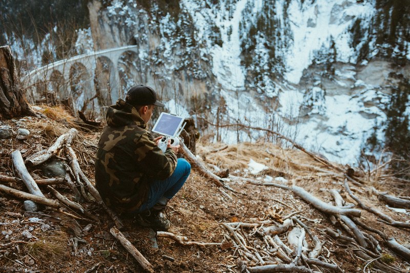 person with a drone controller crouching in a snowy winter forest, controlling a drone 4k