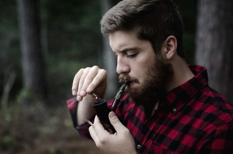hipster man in flannel with a beard lighting a pipe, smoking a pipe 4k