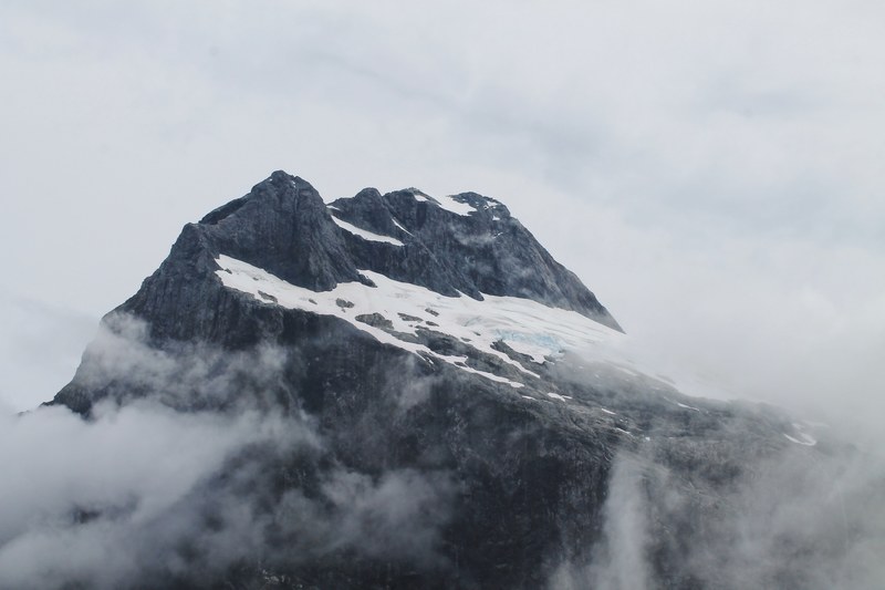 the peak of a mountain covered in snow and surrounded by fog, magnificent milford track 4k