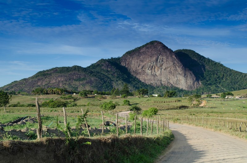 a picturesque landscape with a dirt path winding towards a wooded mountain, winding dirt path in a mountain village 4k