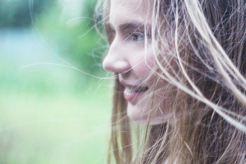 a woman with windswept blonde hair smiles to the side against a blurry green background, nata 4k
