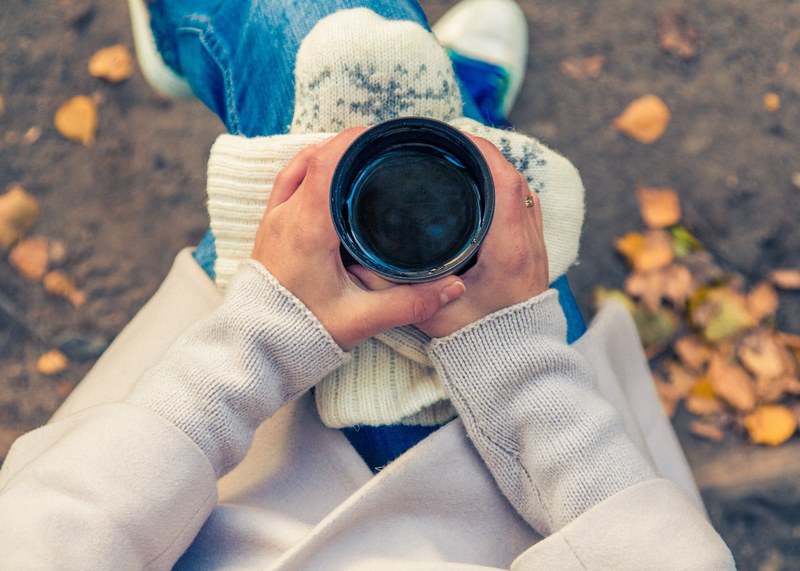 person holds a cup of coffee and mitten on their lap, coffee in autumn 4k