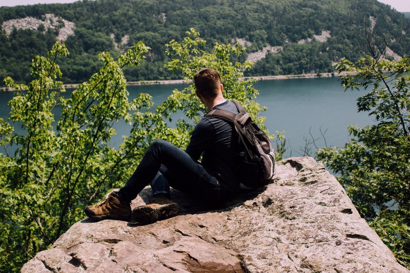 backpacker sits alone on a rocky cliff overlooking a mountain lake, backpacker over a lake 4k