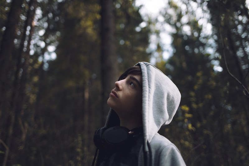person wearing a hoodie and headphones looks up in the woods, young explorer 4k