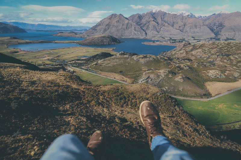 a persons legs dangling off from a hill over mountain lakes in new zealand, sitting over mountain lakes 4k