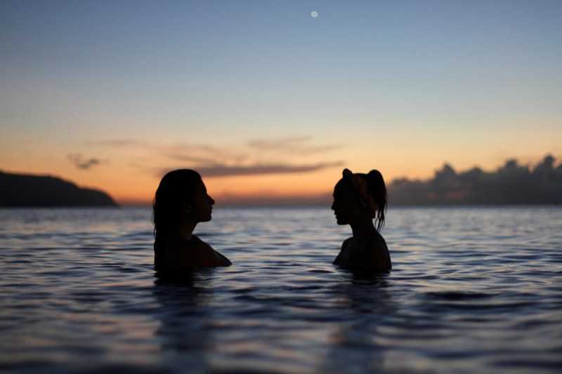 silhouette of two women facing each other while standing in the waters of sunset haleiwa beach, two women ocean sunset 4k