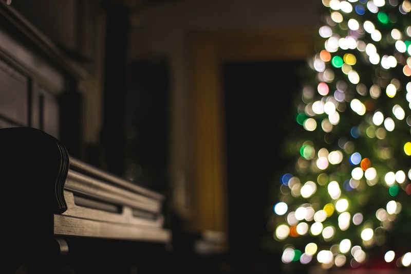 a dim shot of a piano next to a christmas tree with bokeh effect, christmas piano 4k