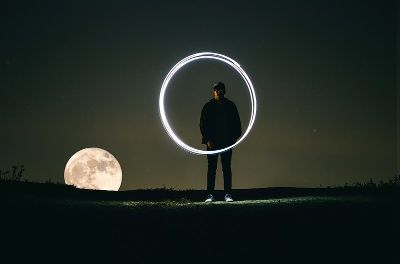 long exposure shot of a man creating a circle of light as the moon rises behind, supermoon in the nightscape 4k