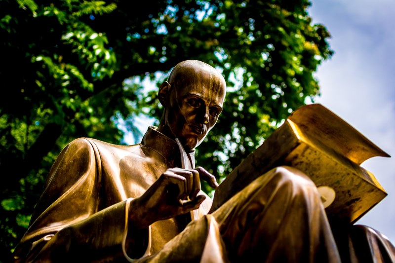 a bronze statue of a man looking down and reading stands outdoors, statue of man reading 4k