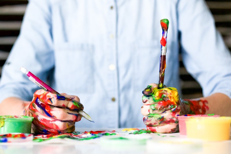 iowa man sits at a messy table while holding paint covered pencil and brush, man holds painted mess 4k