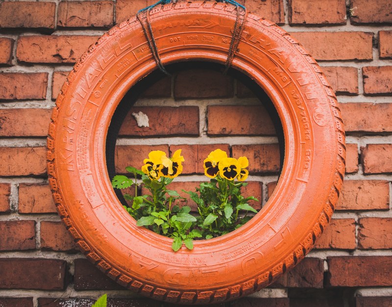 yellow pansies growing in a red tire hanging from a wall, pansies in a tire 4k