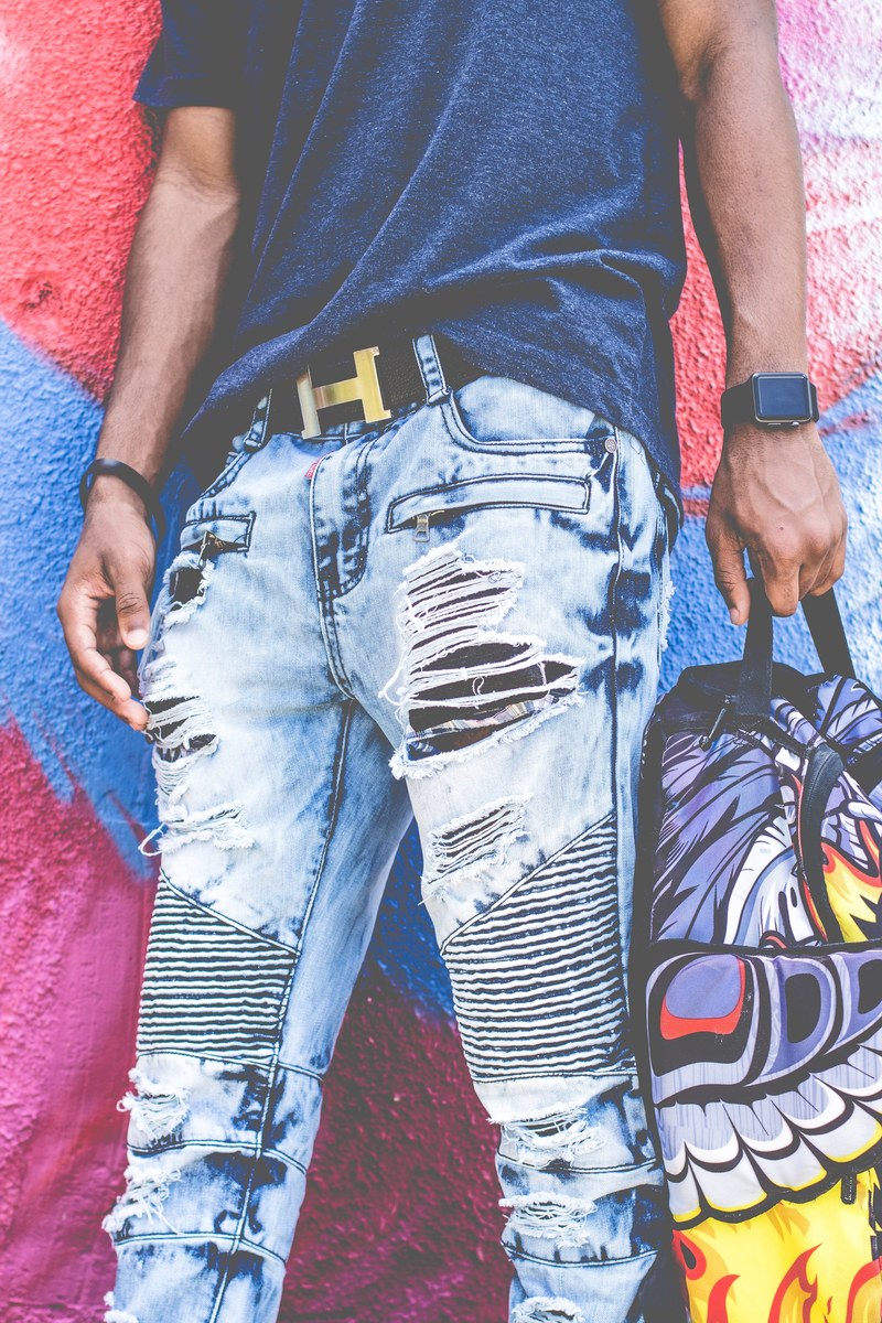 low shot of person wearing ripped jeans and holding a backpack near a mural, urban street clothes 4k