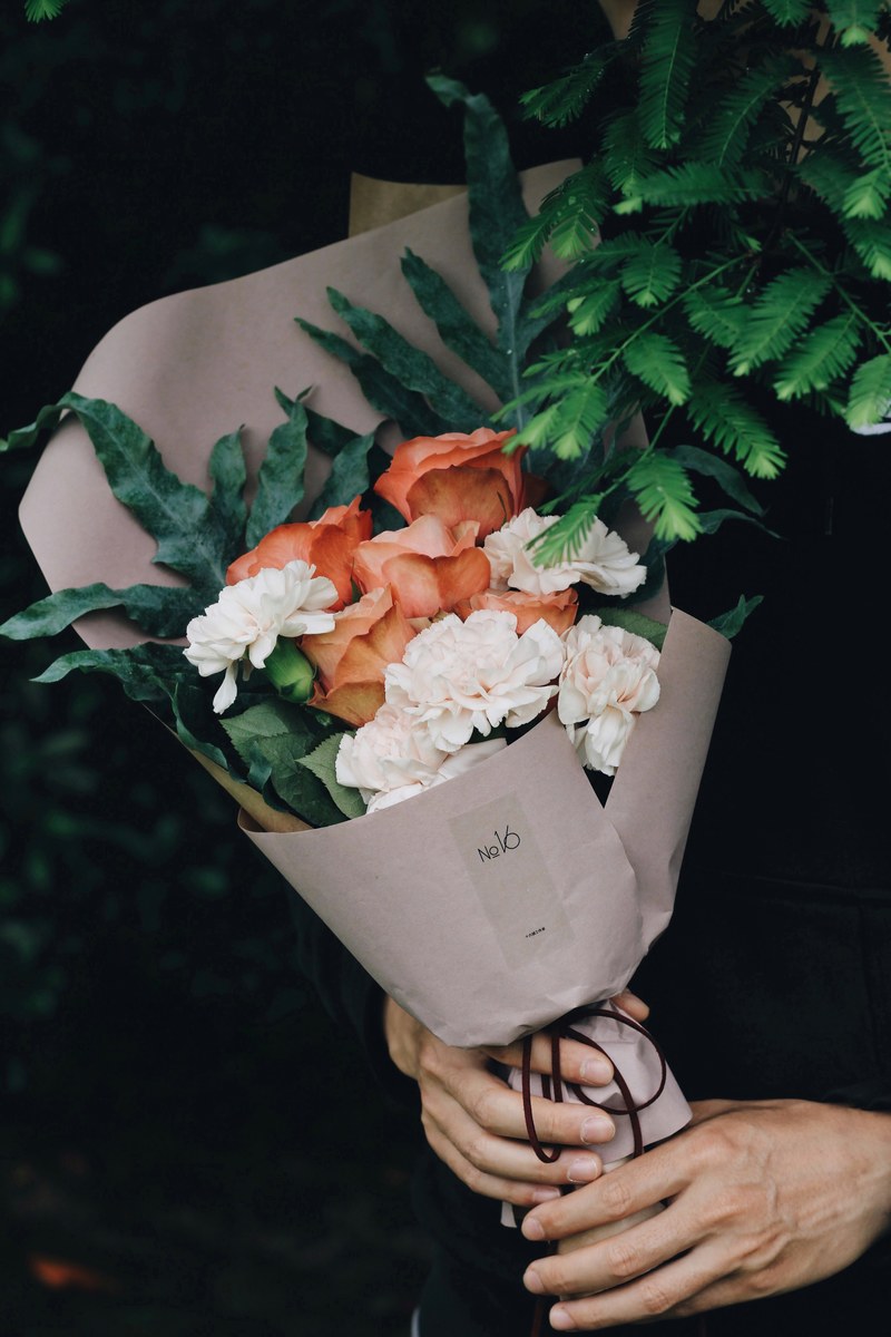 a person holding bouquet of white carnations and pink roses wrapped in decorative paper, paper wrapped bouquet 4k