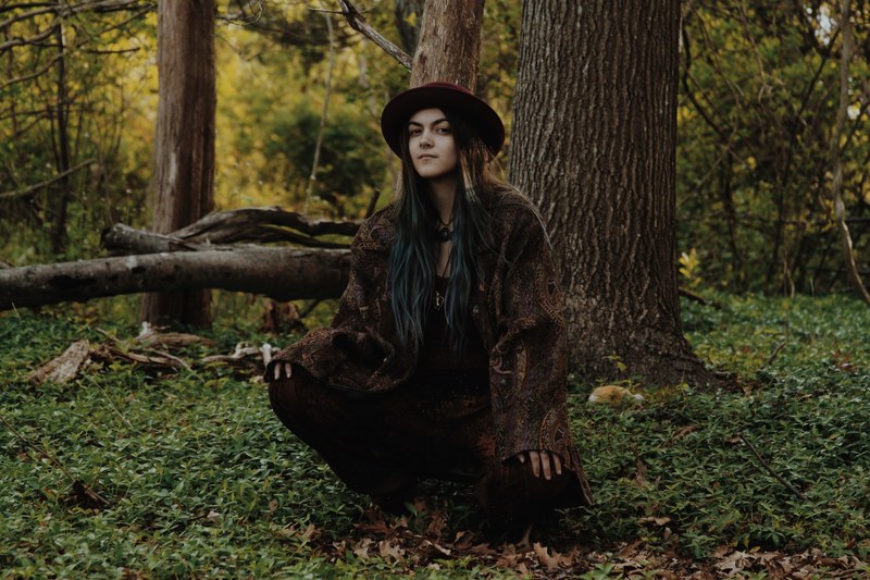a young bohemian woman crouching under a tree in a forest, bohemian woman in the woods 4k
