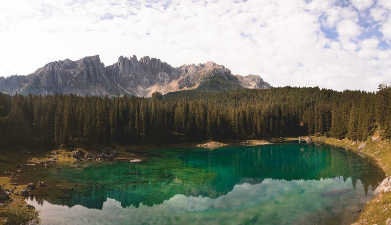 the emerald green lake of carezza near tall granite peaks, trees around a green lake 4k